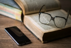open book with a pair of glasses on the page; cell phone on table next to book